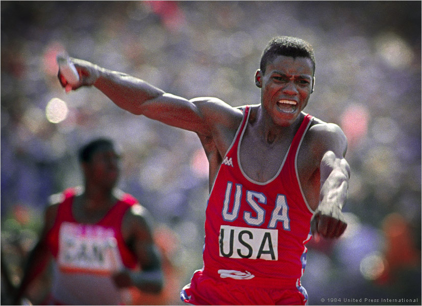 Carl Lewis reacts in joy after seeing a world record time posted on the scoreboard as he crosses the finish line in the men\'s 400 meter relay. Lewis won his 4th gold medal of the games when he anchored the relay team to a 37.83 clocking at the 1984 Olympics in Los Angeles.